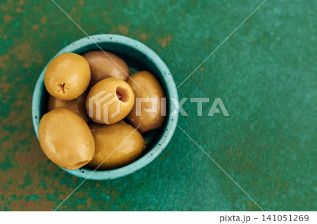 Fresh green olives in a small blue bowl on a textured green surface Fresh green olives in a small blue bowl on a textured green surface 141051269