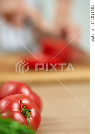 Chef's hands chopping organic ripe red tomatoes on a wooden cutting board, preparing healthy food ingredients Chef's hands chopping organic ripe red tomatoes on a wooden cutting board, preparing healthy food ingredients 141051509