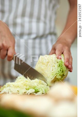 Hands holding a sharp knife and cutting a head of green cabbage into thin shreds for healthy meal preparation Hands holding a sharp knife and cutting a head of green cabbage into thin shreds for healthy meal preparation 141051597