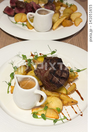 Juicy steak with roasted potatoes and flavorful sauce served on a stylish plate Juicy steak with roasted potatoes and flavorful sauce served on a stylish plate 141051655