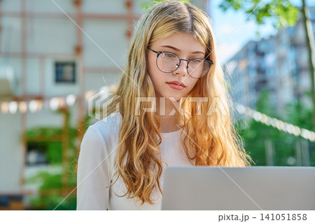 Focused teen girl with glasses looking at laptop screen 141051858