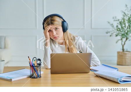 Tired teenage girl in headphones studying with laptop Tired teenage girl in headphones studying with laptop 141051865