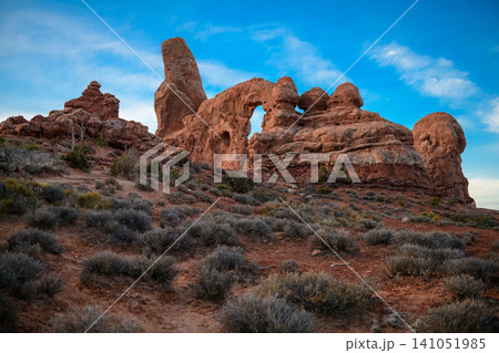 Grand utah landscape reveals distinctive natural arch carved into ancient red rock formation, surrounded by desert plants under clear blue sky, evoking peaceful wonder Grand utah landscape reveals distinctive natural arch carved into ancient red rock formation, surrounded by desert plants under clear blue sky, evoking peaceful wonder 141051985