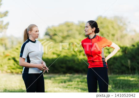 Two women talk during exercise in a park Two women talk during exercise in a park 141052042