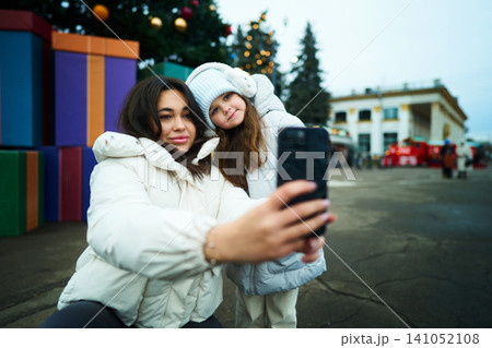 Two girls take a selfie in front of festive decorations at a winter market 141052108