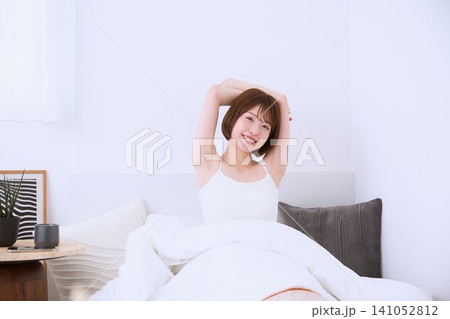 朝ベッドの上で伸びをする笑顔の若い女性 141052812