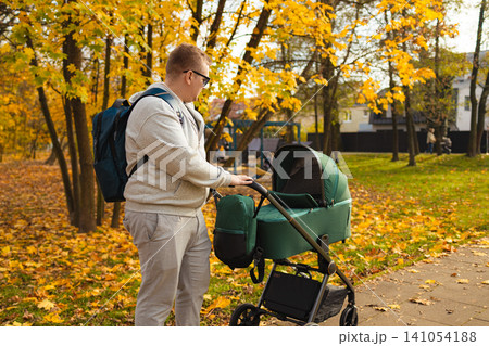 man pushing baby carriage in calm autumn park side view with textile stroller and fabric backpack, peaceful family moment in natural light, for editorial and educational. man pushing baby carriage in calm autumn park side view with textile stroller and fabric backpack, peaceful family moment in natural light, for editorial and educational. 141054188