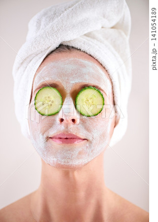 Spa, woman and cucumber facial for skincare in studio with skin mask, organic detox or cosmetics with towel. Model, person or face with fruit for anti aging treatment or self care on white background Spa, woman and cucumber facial for skincare in studio with skin mask, organic detox or cosmetics with towel. Model, person or face with fruit for anti aging treatment or self care on white background 141054189