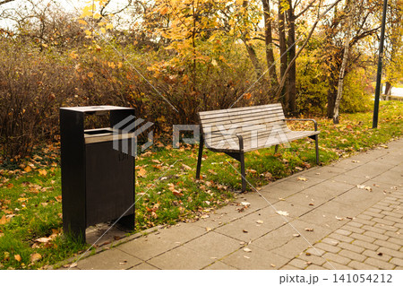 peaceful park bench scene with stationary wooden bench in side view among grass and leaves, green and brown tones, public spaces setting, serene outdoor furniture atmosphere. peaceful park bench scene with stationary wooden bench in side view among grass and leaves, green and brown tones, public spaces setting, serene outdoor furniture atmosphere. 141054212