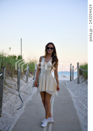 Stylish Woman Walking on Wooden Boardwalk to Beach at Sunset 141054424