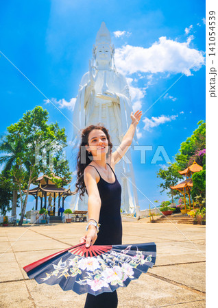 happy Buddhist tourist girl at large statue of Lady Buddha at the famous Linh An pagoda in Dalat in Vietnam. Tourism and attractions in Asia 141054539