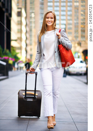 Business woman, luggage and portrait on urban sidewalk with smile, journey and outdoor with pride. Person, happy and baggage on travel in city on metro street by skyscraper buildings in New York 141054723