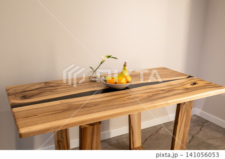 A wooden table displays a bowl of fruit and a small vase with a flower in a clean indoor space. The table stands firmly with sturdy legs A wooden table displays a bowl of fruit and a small vase with a flower in a clean indoor space. The table stands firmly with sturdy legs 141056053