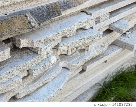 Rough edge of granite stone slabs stacked outdoor grass background closeup Rough edge of granite stone slabs stacked outdoor grass background closeup 141057259