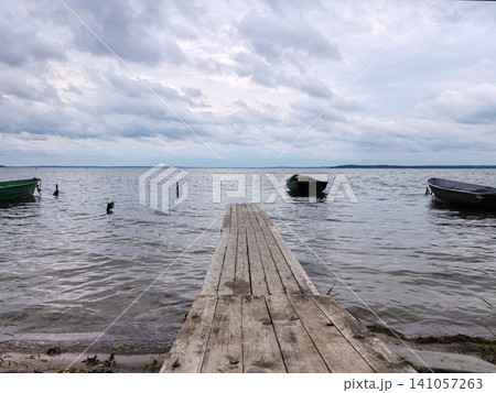 Wooden pier stretching into a large lake with boats under cloudy sky Wooden pier stretching into a large lake with boats under cloudy sky 141057263