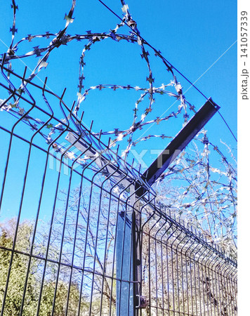 Razor Wire On Security Fence Against Clear Blue Sky Barrier And Protection Concept. Razor Wire On Security Fence Against Clear Blue Sky Barrier And Protection Concept. 141057339