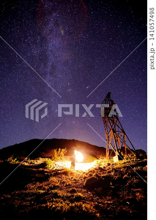 満天の星空と天の川の下の夜の鉱山跡の鉄塔とランタンを持った人物 141057498