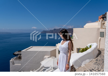 Young woman in white dress looking at Santorini caldera view Young woman in white dress looking at Santorini caldera view 141057560