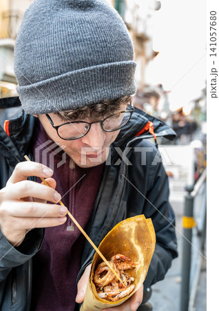 Naples, italy. December 27, 2024. Young man enjoying a delicious cuoppo of mixed fried seafood street food in spaccanapoli, naples, italy Naples, italy. December 27, 2024. Young man enjoying a delicious cuoppo of mixed fried seafood street food in spaccanapoli, naples, italy 141057680