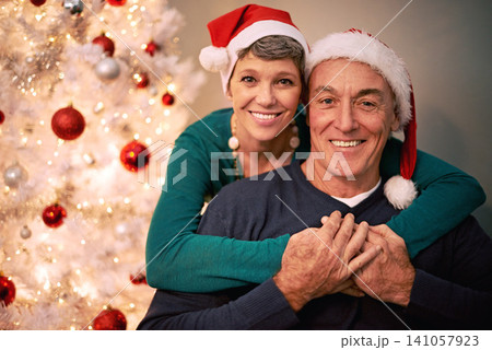 Christmas, portrait and senior couple with love, care and support together in a home on holiday. Tree, retirement and marriage with a smile and hug in a house with celebration and santa hat with joy Christmas, portrait and senior couple with love, care and support together in a home on holiday. Tree, retirement and marriage with a smile and hug in a house with celebration and santa hat with joy 141057923