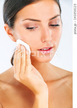 Face, woman and cotton pad for clean skin, makeup removal and skincare for beauty on white background. Product, healthy glow and routine for hygiene, wellness and self care with cosmetics in studio 141058123