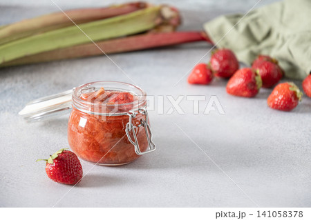 Homemade strawberry rhubarb jam in glass jar on light background 141058378