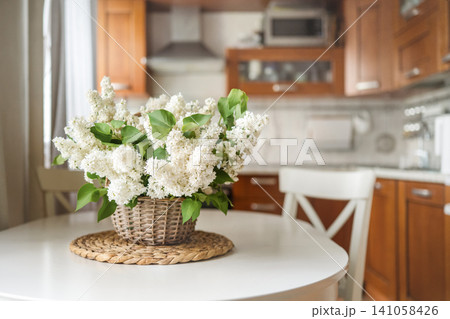 White lilac flowers in wicker basket on kitchen table interior 141058426