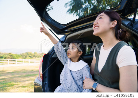 Happy Asian mother and daughter enjoying a family trip while sitting in the open car trunk. 141059105