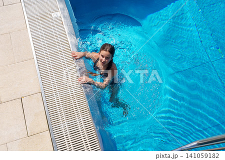 Teen girl holding pool edge in outdoor pool Teen girl holding pool edge in outdoor pool 141059182
