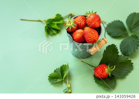 Fresh strawberries spilling from metal bucket on green background Fresh strawberries spilling from metal bucket on green background 141059426