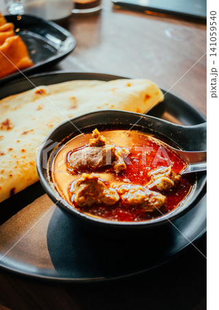 Indian Chicken Curry with Roti Flatbread and Toasted Bread on Wooden Table Indian Chicken Curry with Roti Flatbread and Toasted Bread on Wooden Table 141059540