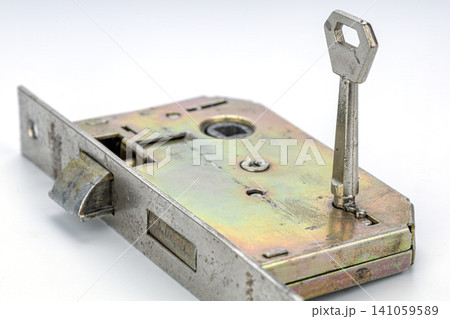 Close-up View of an Antique Metallic Mortise Door Lock Mechanism with a Nickel Plated Key Inserted into the Keyhole Showing Latch Bolt and Internal Components on White Background 141059589
