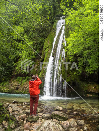 Tourist in orange jacket taking photo of Kaghu waterfall in Georgia. Tourist in orange jacket taking photo of Kaghu waterfall in Georgia. 141059600