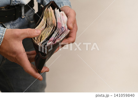Man closes wallet full of cash, symbolizing completion of payment, savings, and income management. Man closes wallet full of cash, symbolizing completion of payment, savings, and income management. 141059840