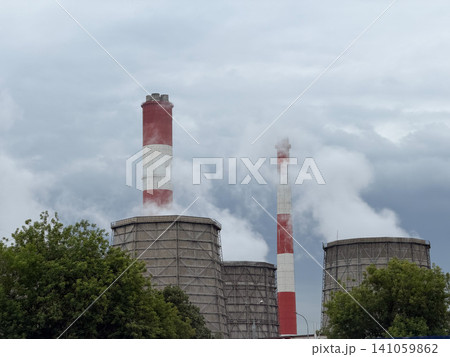 Cooling towers and industrial smokestacks rise above trees with steam drifting across power plant. Energy, electricity generation, industry, infrastructure, utilities, engineering, environment Cooling towers and industrial smokestacks rise above trees with steam drifting across power plant. Energy, electricity generation, industry, infrastructure, utilities, engineering, environment 141059862
