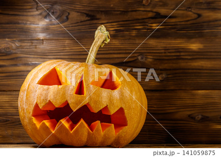 Spooky Halloween pumpkin jack-o-lantern on a wooden background Spooky Halloween pumpkin jack-o-lantern on a wooden background 141059875