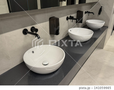 Modern washbasins with wall mounted faucets and soap dispensers in minimalist public restroom interior. Hygiene, sanitation, healthcare, facility management, cleanliness, hospitality, workplace Modern washbasins with wall mounted faucets and soap dispensers in minimalist public restroom interior. Hygiene, sanitation, healthcare, facility management, cleanliness, hospitality, workplace 141059985