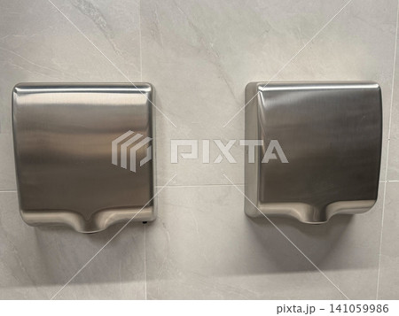 Stainless steel hand dryers mounted on tiled wall in modern public restroom interior. Hygiene, sanitation, facility management, touchless technology, cleanliness, healthcare, hospitality Stainless steel hand dryers mounted on tiled wall in modern public restroom interior. Hygiene, sanitation, facility management, touchless technology, cleanliness, healthcare, hospitality 141059986
