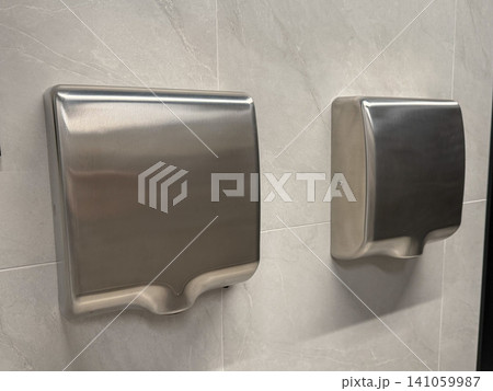 Stainless steel hand dryers mounted on tiled wall in modern public restroom interior. Hygiene, sanitation, facility management, touchless technology, cleanliness, healthcare, hospitality Stainless steel hand dryers mounted on tiled wall in modern public restroom interior. Hygiene, sanitation, facility management, touchless technology, cleanliness, healthcare, hospitality 141059987