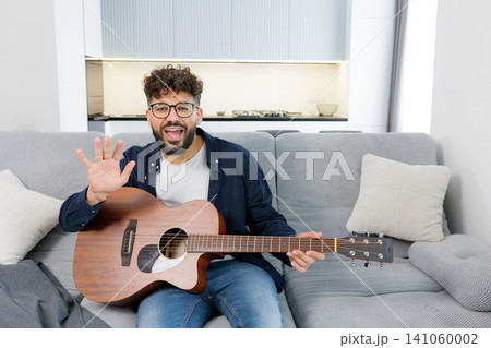 Man waving, holding acoustic guitar, playing music at home Man waving, holding acoustic guitar, playing music at home 141060002