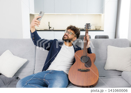 Man taking selfie with acoustic guitar on sofa Man taking selfie with acoustic guitar on sofa 141060006