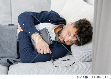 Man napping on sofa holding book at home Man napping on sofa holding book at home 141060017