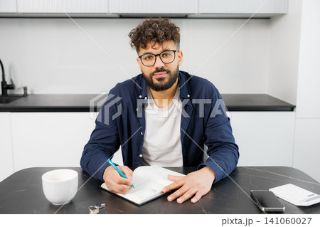 Young man planning personal finances at home kitchen 141060027