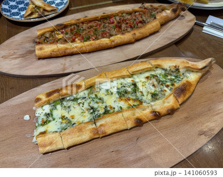 Traditional Turkish pide with cheese and minced meat is served on wooden boards in restaurant. Turkish cuisine, gastronomy, local food, hospitality, culinary tourism, dining, travel, authentic cuisine Traditional Turkish pide with cheese and minced meat is served on wooden boards in restaurant. Turkish cuisine, gastronomy, local food, hospitality, culinary tourism, dining, travel, authentic cuisine 141060593