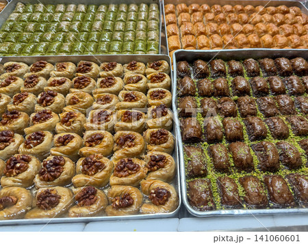 Traditional Turkish baklava assortment with pistachio and walnut filling displayed in metal trays at pastry shop. Turkish cuisine, dessert, confectionery, food culture, gastronomy, retail, travel Traditional Turkish baklava assortment with pistachio and walnut filling displayed in metal trays at pastry shop. Turkish cuisine, dessert, confectionery, food culture, gastronomy, retail, travel 141060601