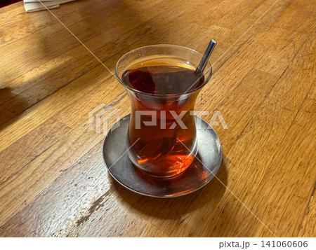 Traditional Turkish tea served in tulip shaped glass on metal saucer with spoon over wooden table. Turkish culture, hospitality, beverage, cafe, lifestyle, travel, food culture, refreshment Traditional Turkish tea served in tulip shaped glass on metal saucer with spoon over wooden table. Turkish culture, hospitality, beverage, cafe, lifestyle, travel, food culture, refreshment 141060606