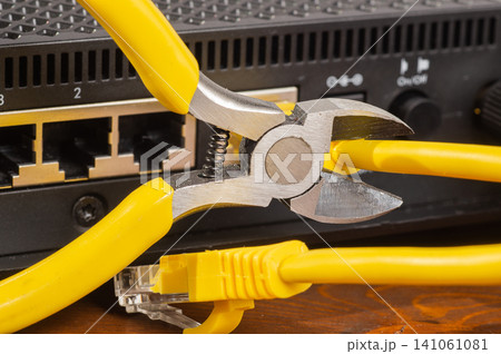 Pliers cutting a yellow ethernet cable plugged into a network router port close up. Pliers cutting a yellow ethernet cable plugged into a network router port close up. 141061081