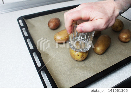 A male cook crushes potatoes with a glass. Baked potatoes. 141061306
