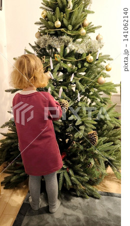 little girl turning away decorating christmas tree dressed in dress christmas tree decor in room 141062140