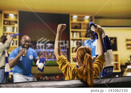 Close up of smiling football supporters on sofa celebrating together at home. Back view of happy soccer fans raising arms in excitement after positive match result Close up of smiling football supporters on sofa celebrating together at home. Back view of happy soccer fans raising arms in excitement after positive match result 141062330